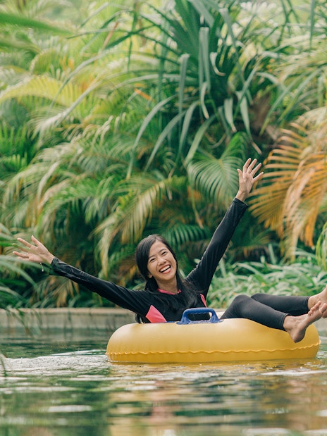 Girl floating on a ring in lazy river at Waterbom Bali surrounded by lush greenery.