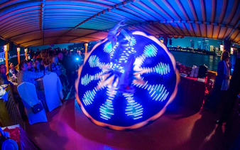 Tanoura dancer performing on Alexandra VIP Dhow Cruise with city skyline in background.