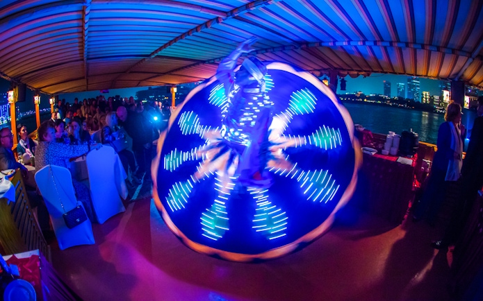 Tanoura dancer performing on Alexandra VIP Dhow Cruise with city skyline in background.