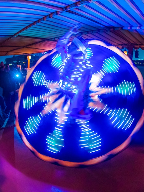 Tanoura dancer performing on Alexandra VIP Dhow Cruise with city skyline in background.
