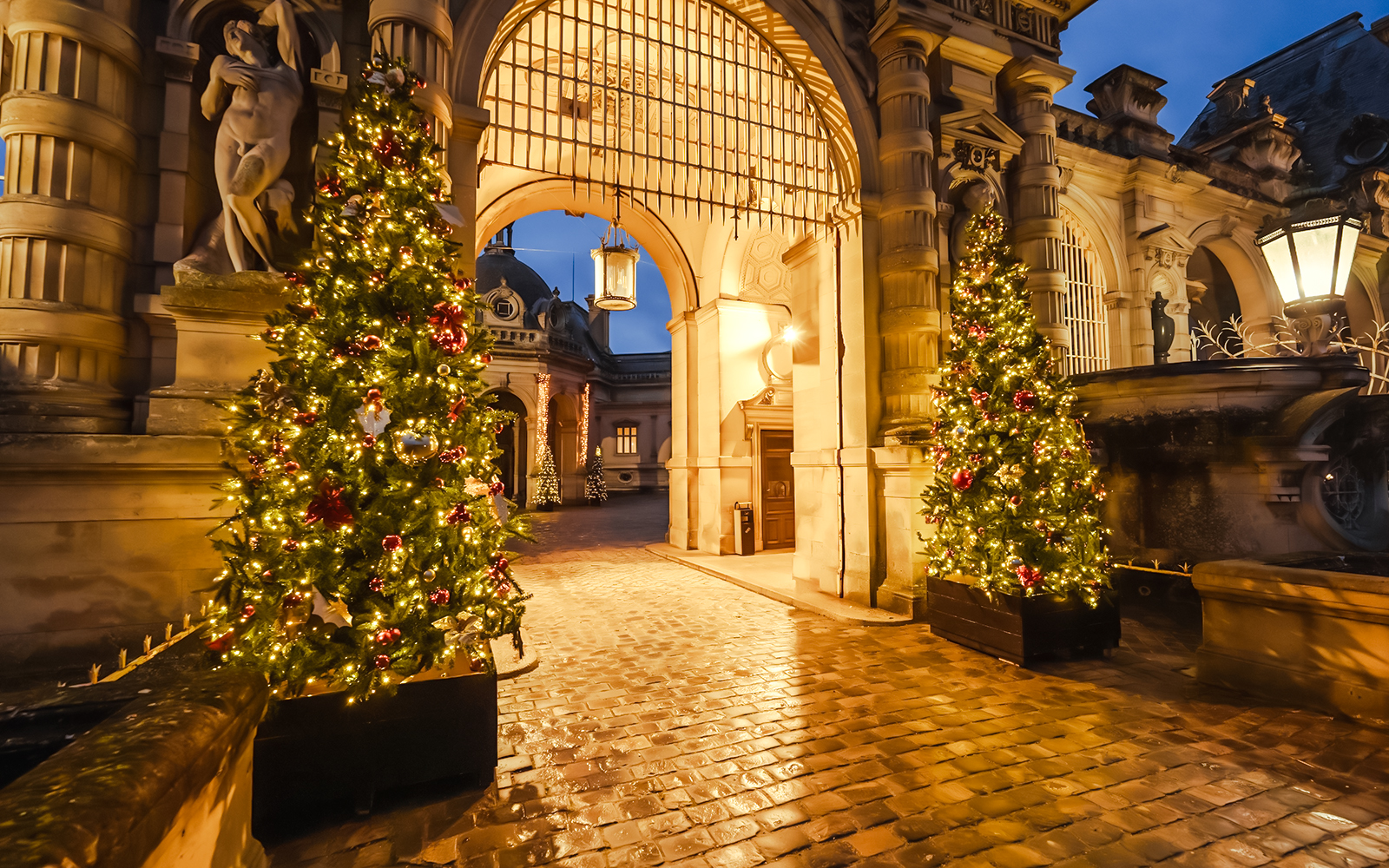 Chateau of Chantilly entrance with festive Christmas trees illuminated at night.