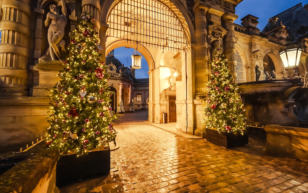 Chateau of Chantilly entrance with festive Christmas trees illuminated at night.