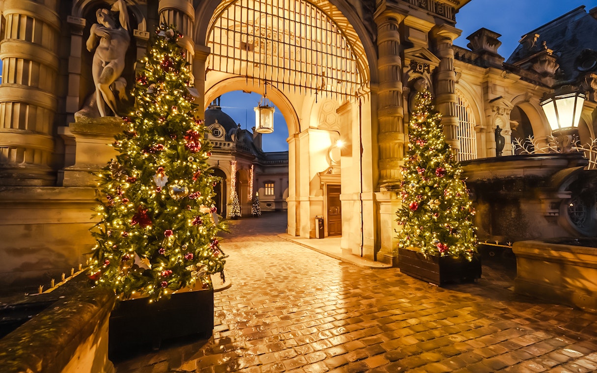 Chateau of Chantilly entrance with festive Christmas trees illuminated at night.