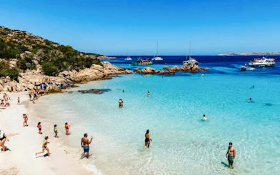 Motorboats anchored near a beach in La Maddalena Archipelago, people swimming and relaxing.