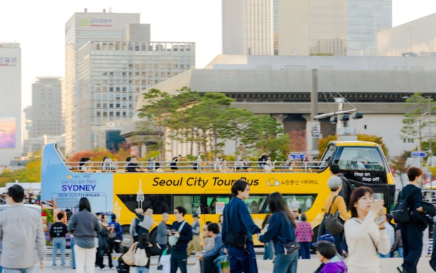 Yellow double-decker bus on a city tour in Dongdaemun, Seoul, with passengers on the upper deck.