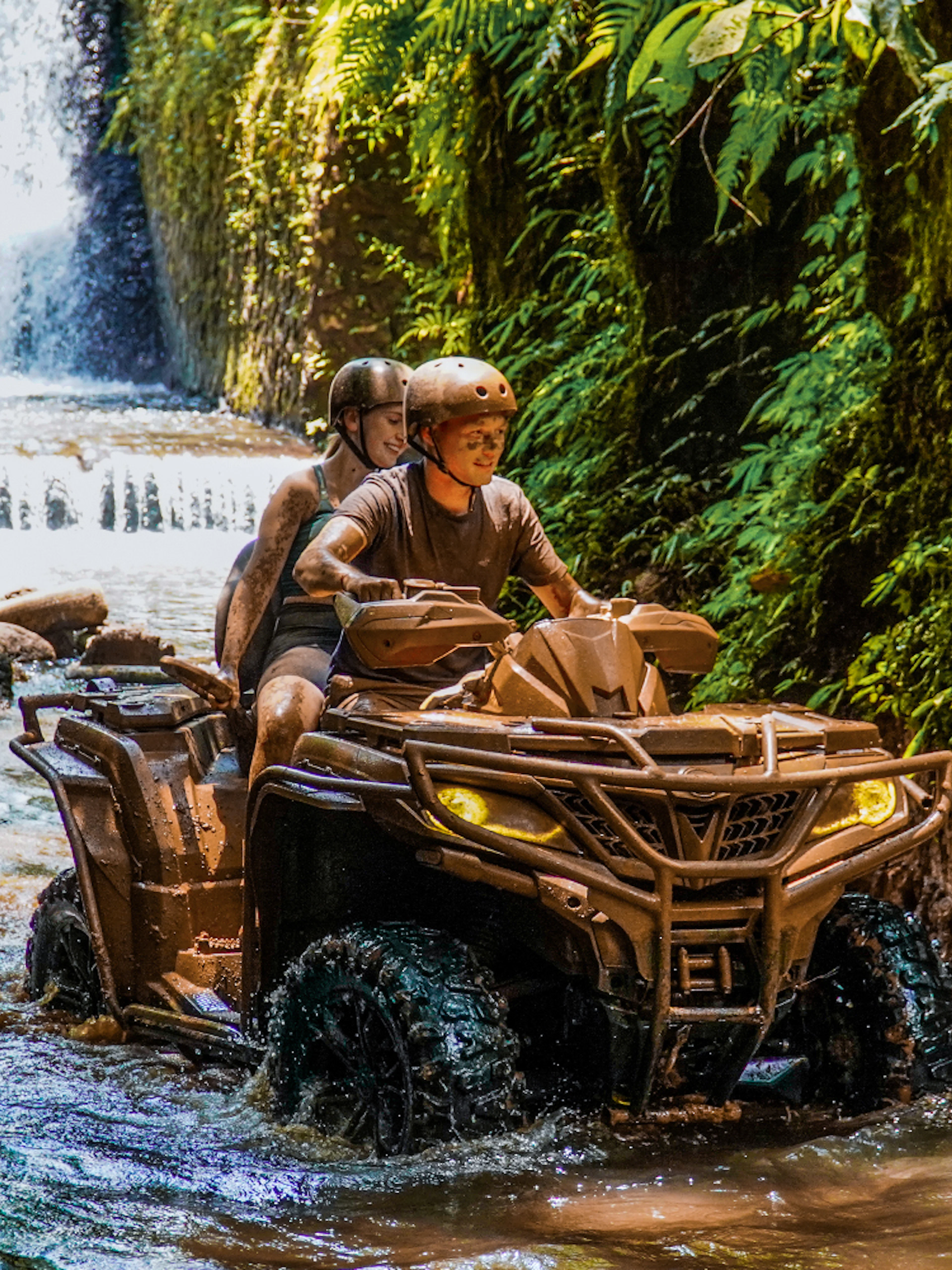 ATV riders navigating a stream near a waterfall in Ubud's lush jungle.