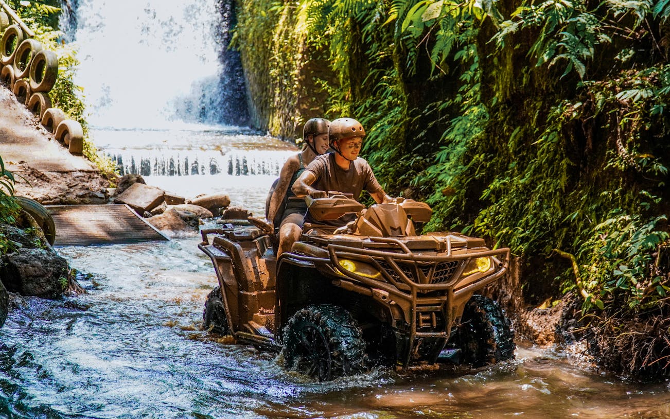 ATV riders navigating a stream near a waterfall in Ubud's lush jungle.
