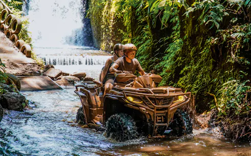 ATV riders navigating a stream near a waterfall in Ubud's lush jungle.