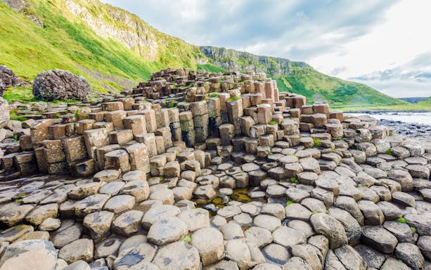 Giant's Causeway basalt columns with green cliffs in Northern Ireland.