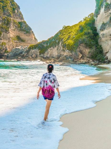 Tourist walking along Diamond Beach with turquoise waters, Nusa Penida Island, Bali.