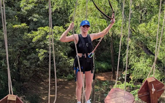 Person navigating high-elevation ropes course with safety gear in forest setting.