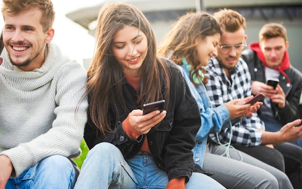 Group of people sitting outdoors, smiling and looking at their phones.