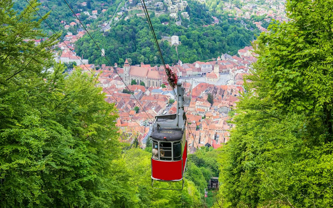 Cable car descending over Brașov with cityscape and forest view, Romania.