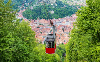 Cable car descending over Brașov with cityscape and forest view, Romania.