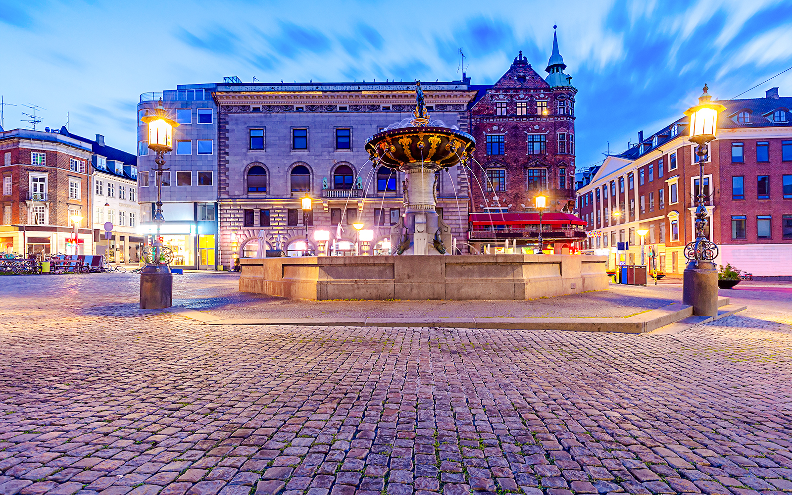 Amagertorv Square fountain in Copenhagen at dusk with historic buildings in the background.
