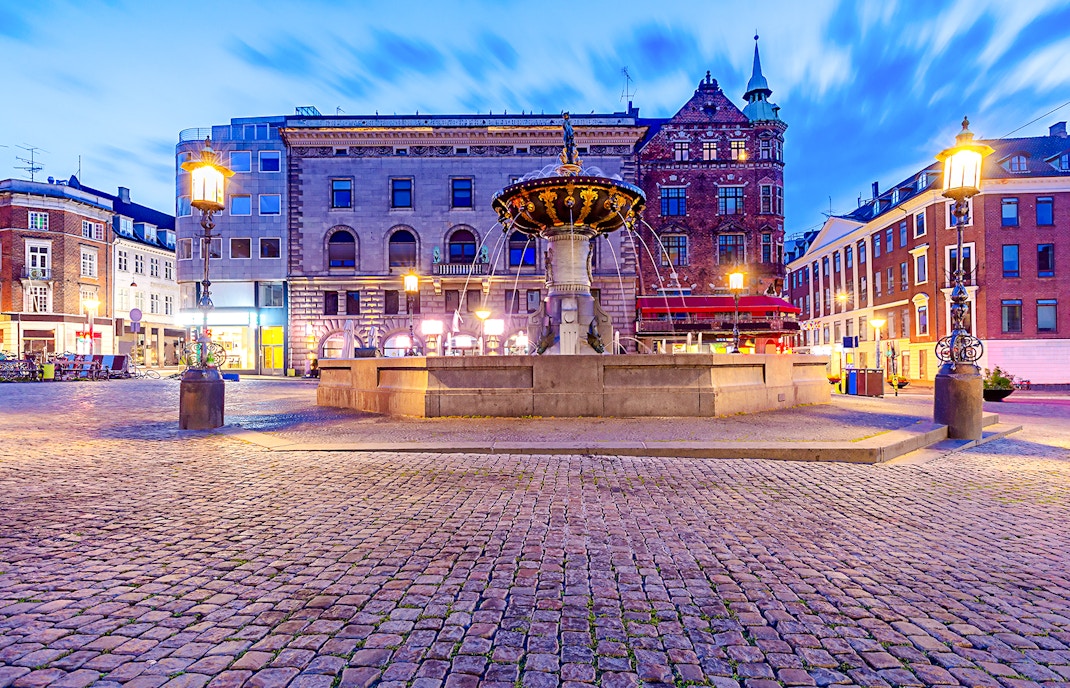 Amagertorv Square fountain in Copenhagen at dusk with historic buildings in the background.