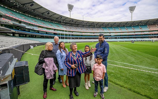 Tour group at Melbourne Cricket Ground with guide explaining features.