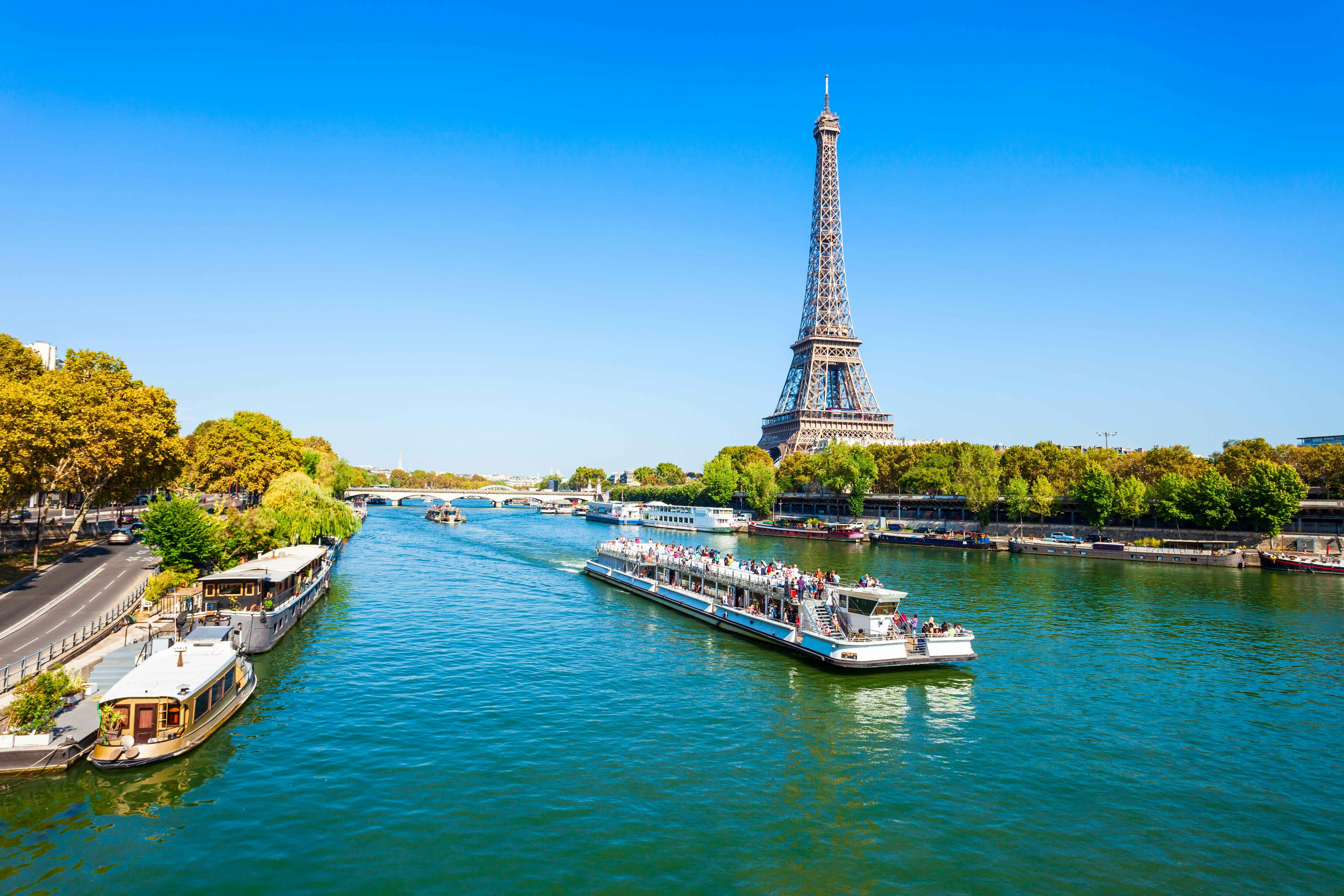 Seine River cruise boat with passengers dining, Paris landmarks in background.