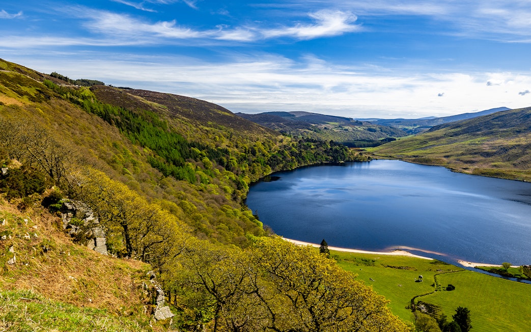 Wicklow Mountains view with lush greenery and a serene lake under a blue sky.