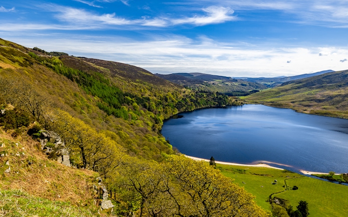 Wicklow Mountains view with lush greenery and a serene lake under a blue sky.