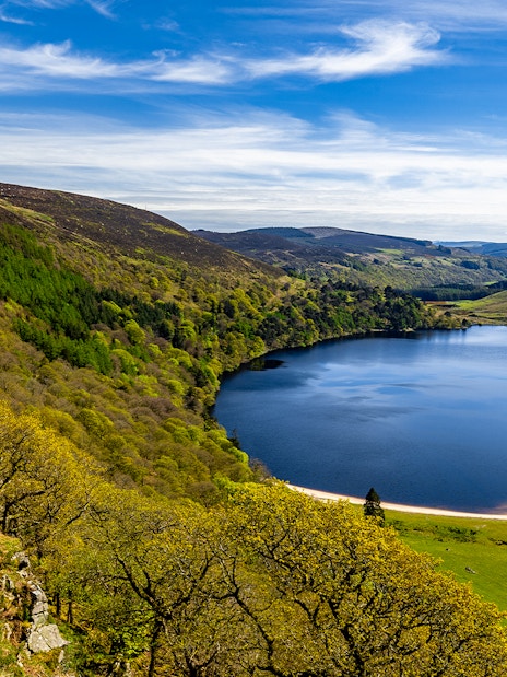 Wicklow Mountains view with lush greenery and a serene lake under a blue sky.