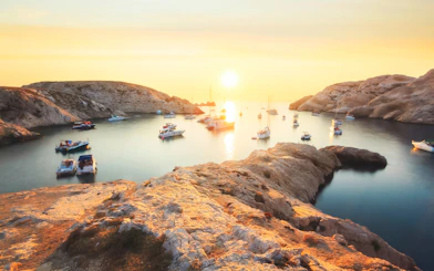 Boats anchored in a rocky cove during sunset on a Marseille dinner cruise.