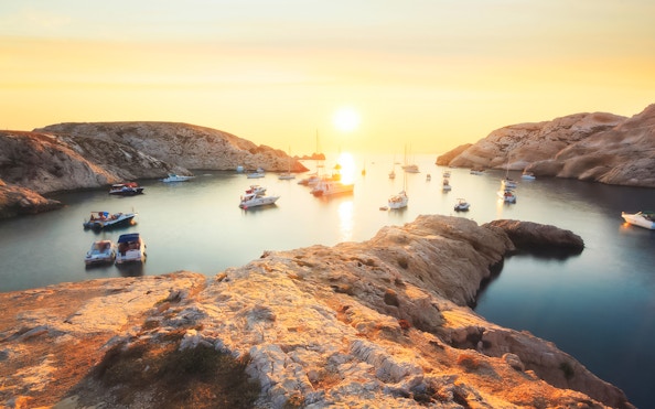 Boats anchored in a rocky cove during sunset on a Marseille dinner cruise.