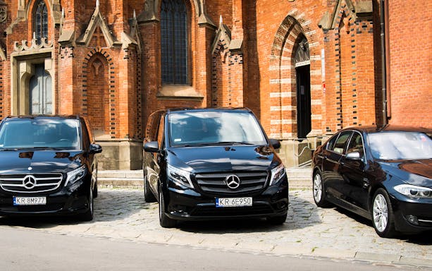 Black Mercedes vehicles parked in front of a historic brick building in Krakow for Balice Airport transfer.
