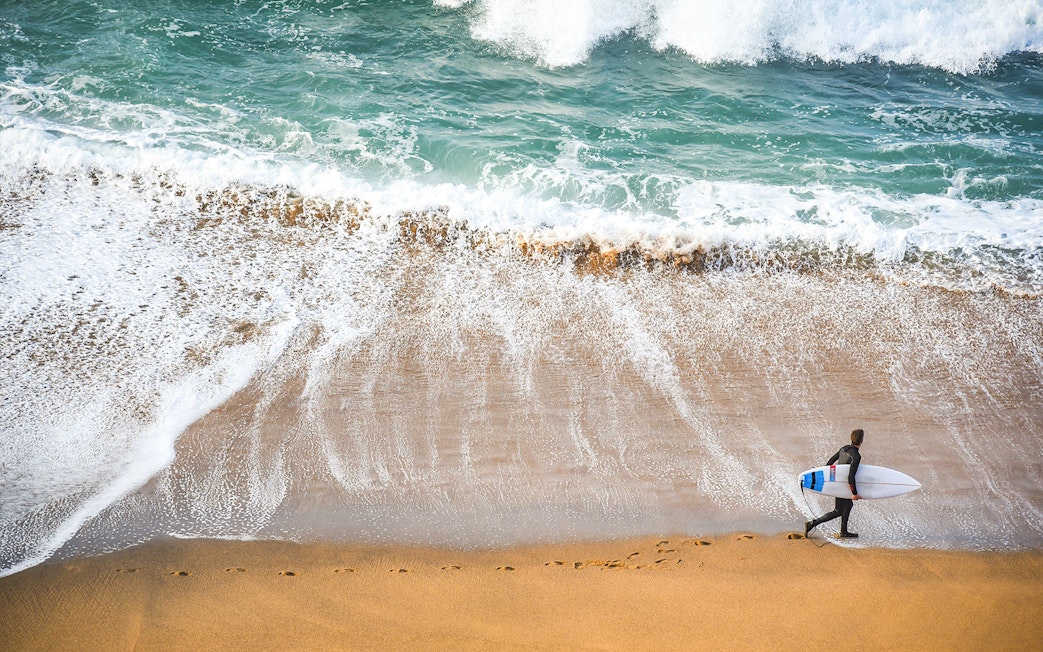 Surfer walking along the beach on the Great Ocean Road, Australia.