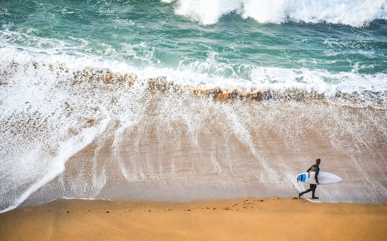 Surfer walking along the beach on the Great Ocean Road, Australia.
