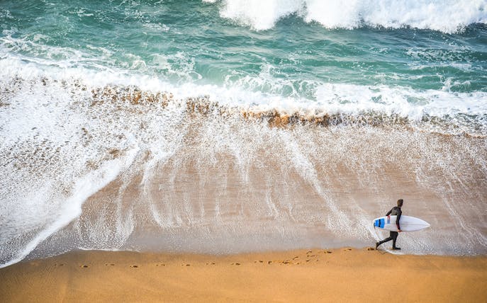 Surfer walking along the beach on the Great Ocean Road, Australia.