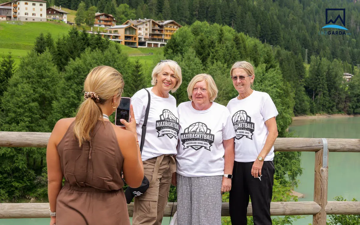 Tourists posing for a photo with a scenic view of the Dolomites and a lake in the background.