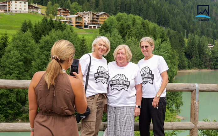 Tourists posing for a photo with a scenic view of the Dolomites and a lake in the background.