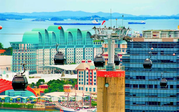 Cable cars over Sentosa Island, Singapore with cityscape and ocean in the background.