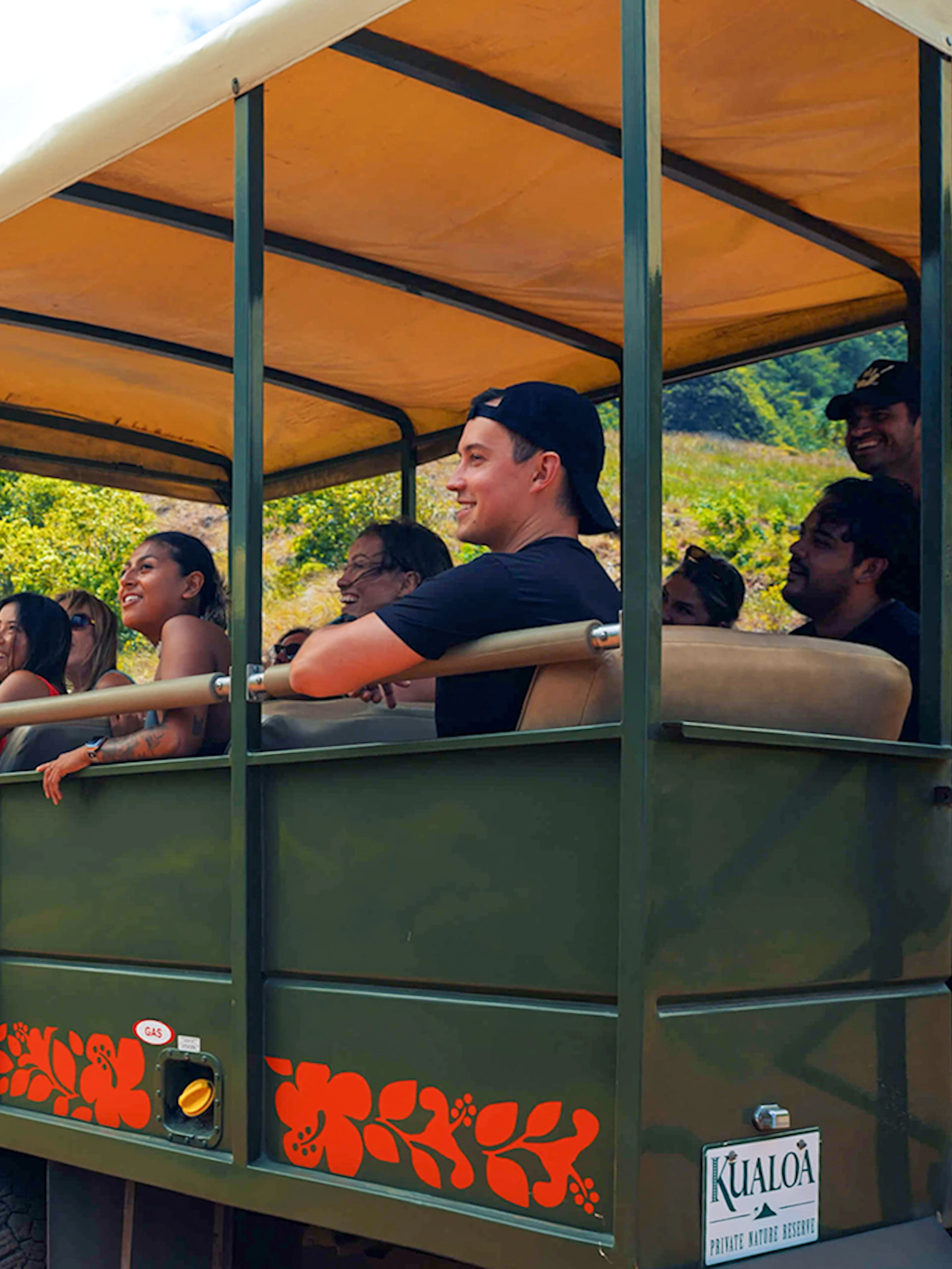 Tourists on a safari vehicle exploring Kualoa Ranch, Hawaii with lush mountains in the background.