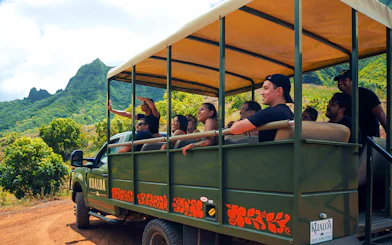 Tourists on a safari vehicle exploring Kualoa Ranch, Hawaii with lush mountains in the background.