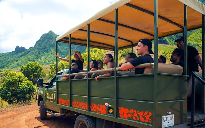Tourists on a safari vehicle exploring Kualoa Ranch, Hawaii with lush mountains in the background.