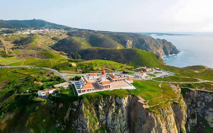 Cape Roca lighthouse on cliff edge overlooking ocean, Cabo da Roca, Portugal.