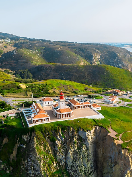 Cape Roca lighthouse on cliff edge overlooking ocean, Cabo da Roca, Portugal.