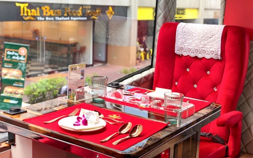Luxurious dining setup inside a Thai Bus Food Tour with red velvet seating and tableware.