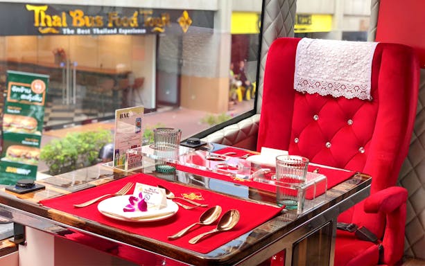 Luxurious dining setup inside a Thai Bus Food Tour with red velvet seating and tableware.