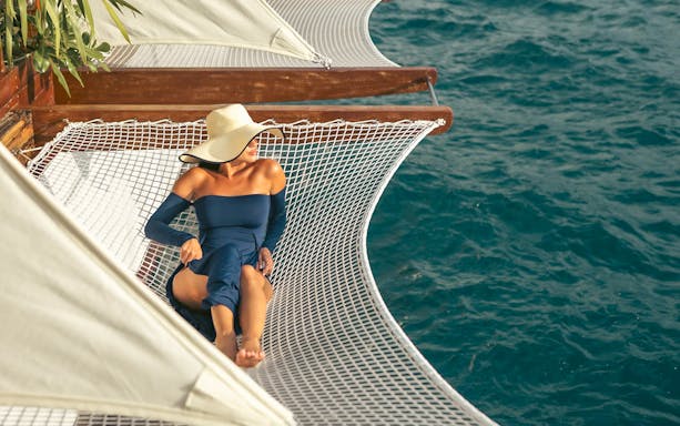 Person relaxing on a net hammock over the ocean at Yona Beach Club, Phuket.