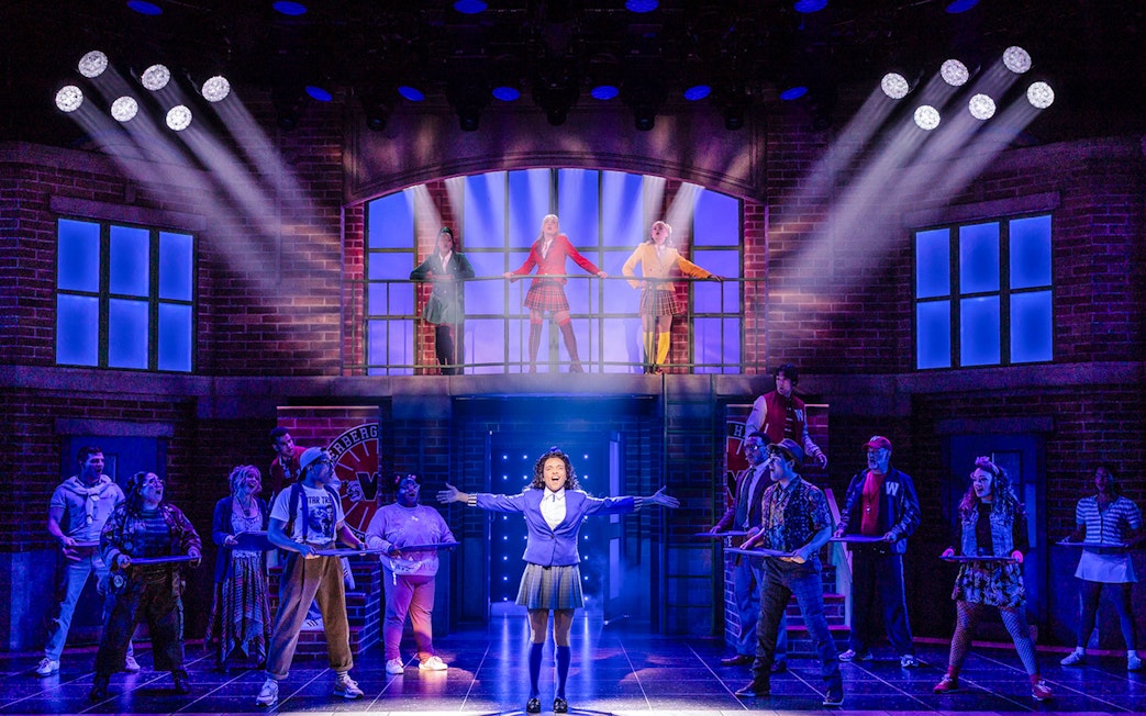 Cast performing a scene from Heathers: The Musical on stage with dramatic lighting.