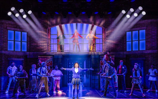 Cast performing a scene from Heathers: The Musical on stage with dramatic lighting.