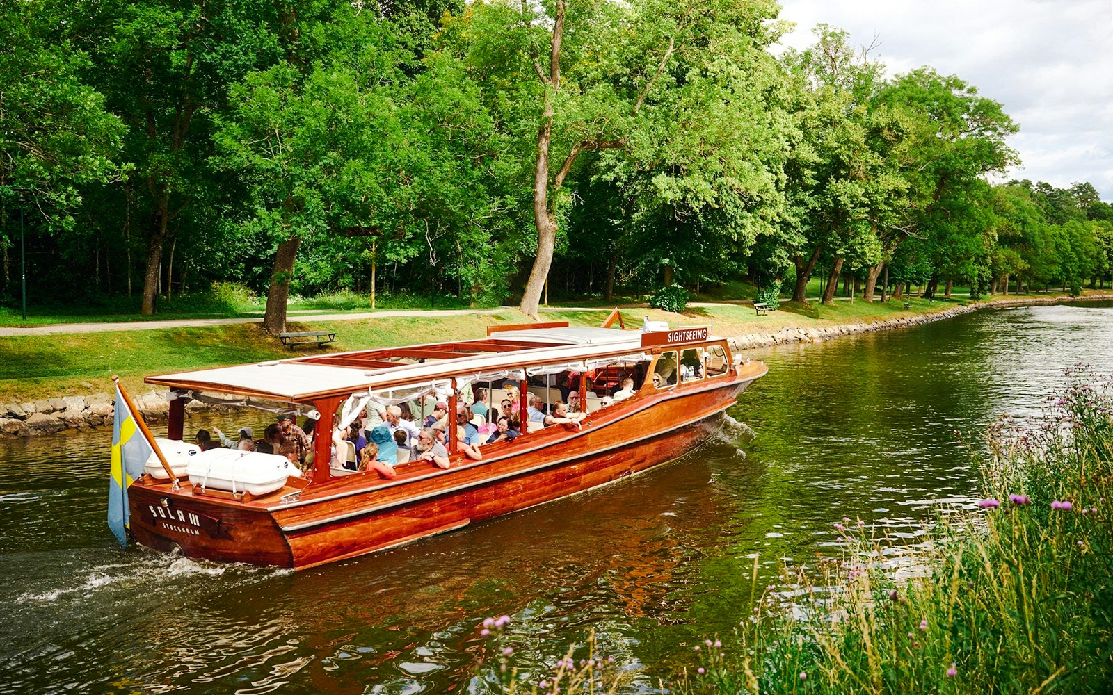 Classic wooden boat cruising through Stockholm Archipelago with passengers enjoying the scenic view.