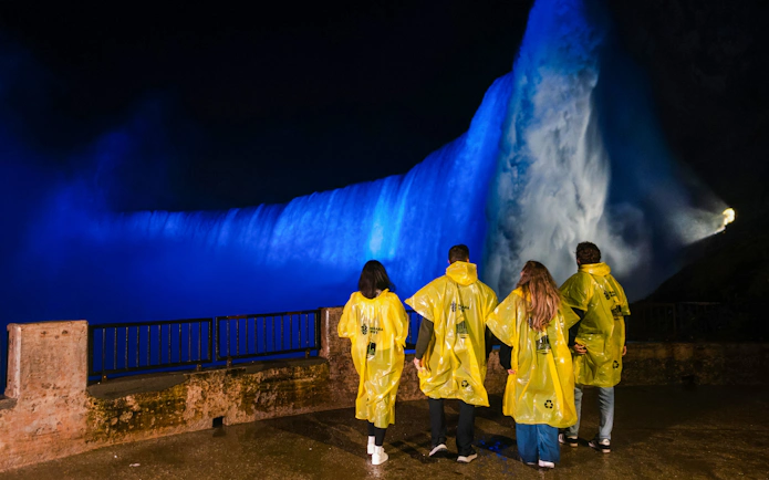 Visitors in yellow ponchos view illuminated Niagara Falls at night during the Journey Behind the Falls tour.