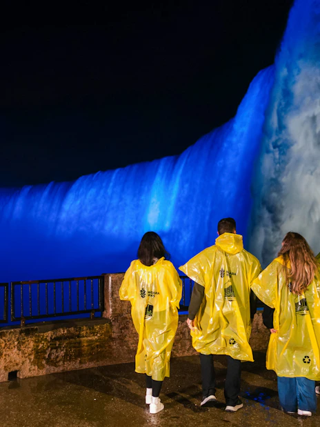 Visitors in yellow ponchos view illuminated Niagara Falls at night during the Journey Behind the Falls tour.