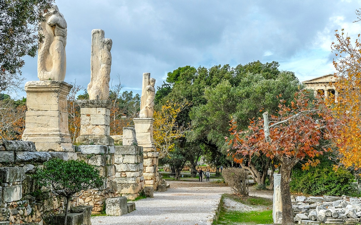 Odeon of Agrippa statues in Ancient Agora, Athens, with trees and ruins in the background.