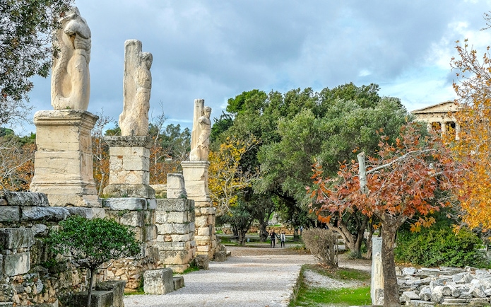 Odeon of Agrippa statues in Ancient Agora, Athens, with trees and ruins in the background.