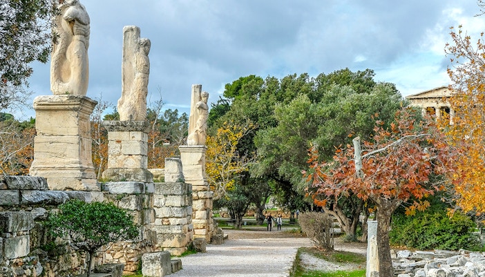Odeon of Agrippa statues in Ancient Agora, Athens, with trees and ruins in the background.